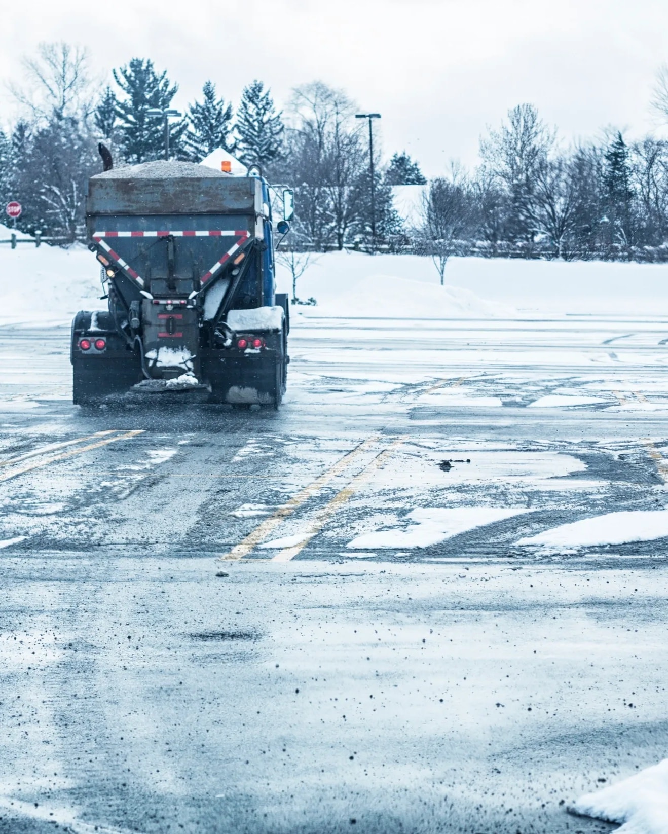 Truck spreading ice-melting salt across a winter parking lot